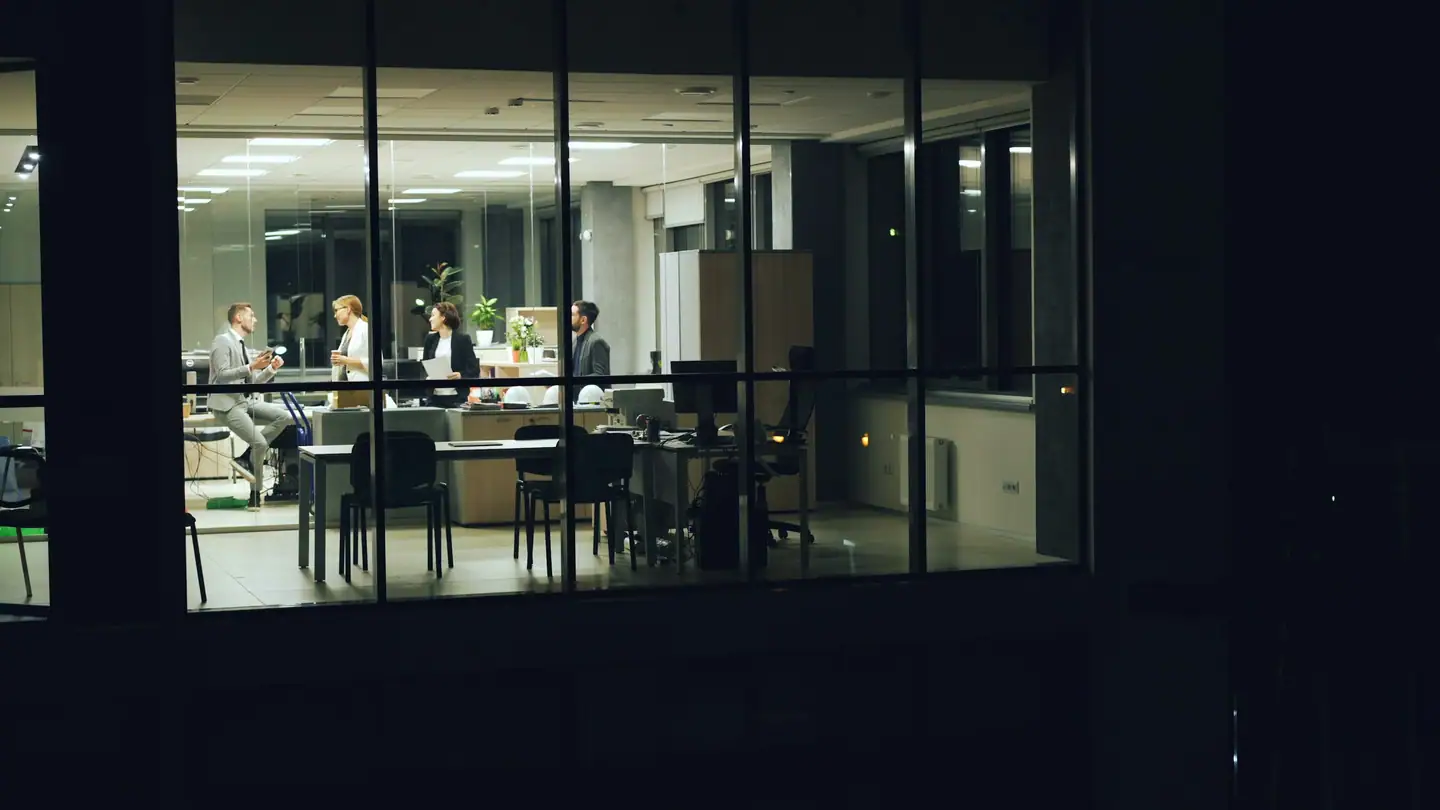 Colleagues working together in a glass-walled office at night